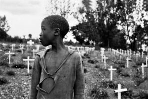 Un enfant rwandais au premier plan, un cimetière de croix blanches au second plan.