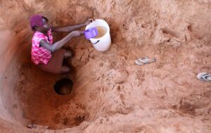 Collecte d'eau par une femme africaine au fond d'un trou creusé à même la terre.